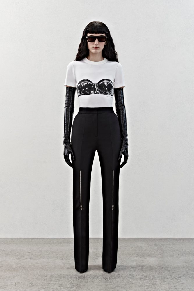 A t-shirt in white cotton jersey with a black trompe l’oeil bustier print and high-waisted trousers in black grain de poudre with silver metal zip detailing.