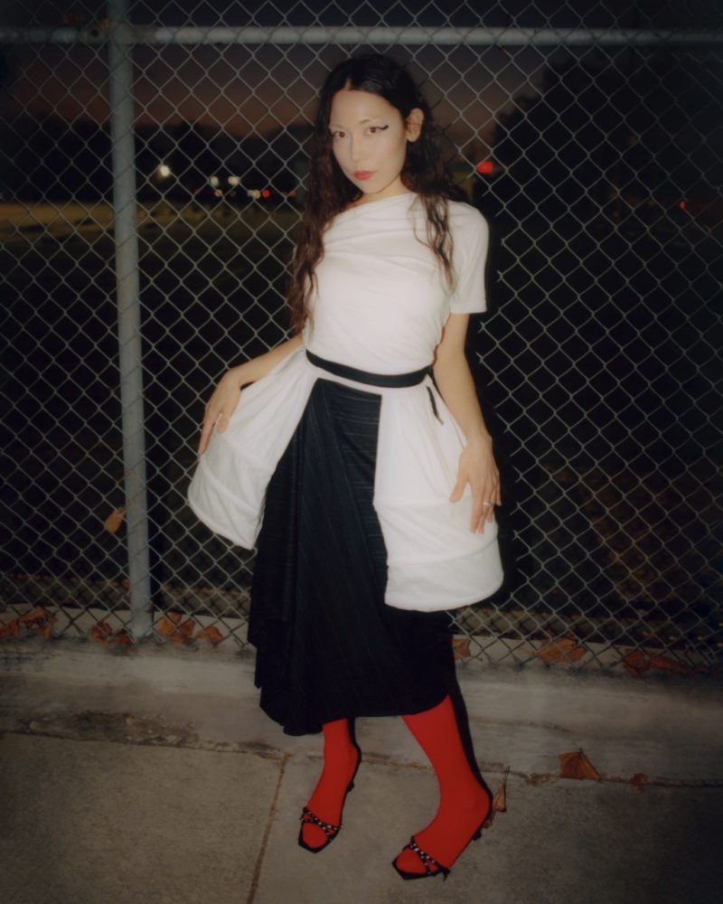 Sasami wears GIVENCHY top available at FWRD, COS skirt, SERPENTI shoes, PYRRHA ring, MENĒ ring, and stylist's own pannier. Written and Produced by BJ Panda Bear. Photographed by Andrew Friendly. Styled by Britton Litow. Hair: Paul Rizzo using Bumble and Bumble. Makeup: Nichole Servin using Westman Atelier and Rare Beauty. Stylist Assistant: Maddie Collins.